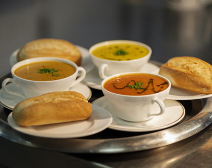Three bowls of soup with bread rolls on a tray.