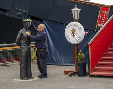A Facilities Officer wiping down a statue of an ex-Yachtsman, Norrie, on the quayside.