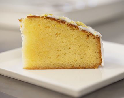 A slice of lemon drizzle cake on a white plate.